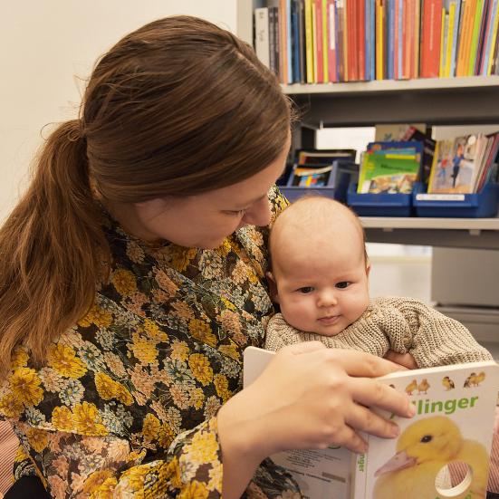 Billede af en mor, der sidder og kigger i en bod med sin baby