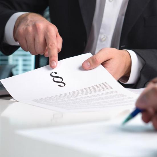 Overkroppen af en mand i jakkesæt der peger på et dokument med paragraffer