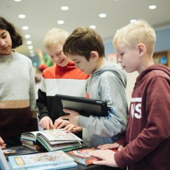 Fire børn der står samlet om en åben bog.