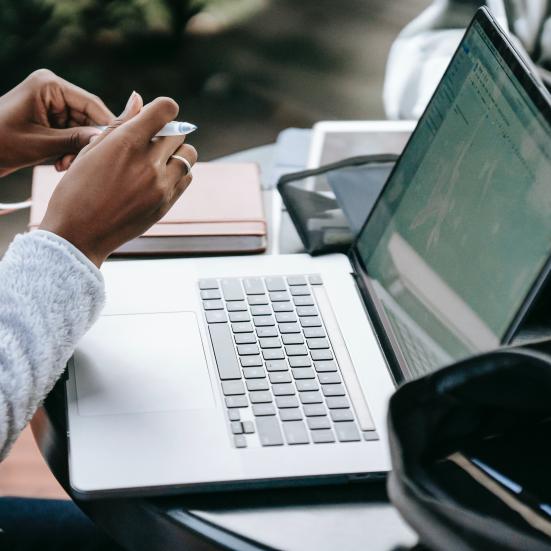 Armene af en ung person, der sidder foran en opslået labtop.