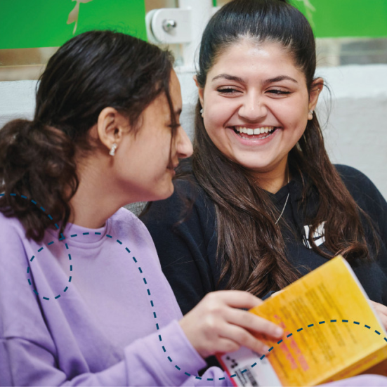 En pige og en kvinde der sidder grinende ved siden af hinanden med hver siden bog