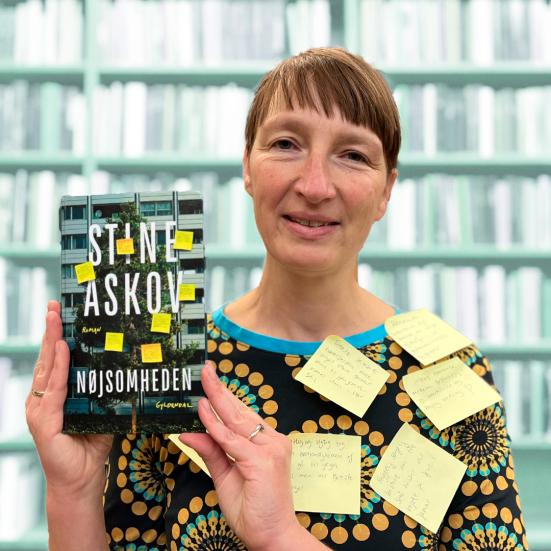 Litteraturformidler Bettina Schnegelsberg-Laursen holder bogen 'Nøjsomheden'. Bettina har seks gule post-it sedler på sig, så hun matcher forsiden af bogen