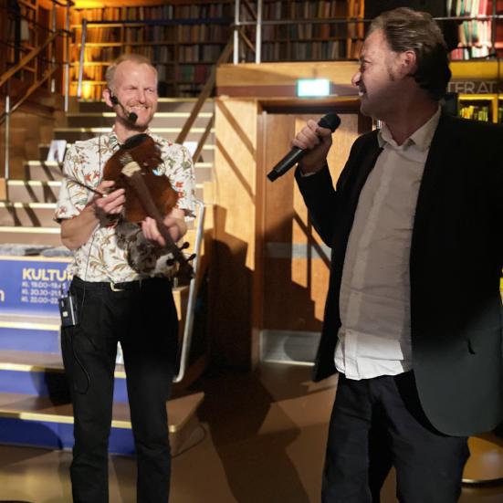 Knud Romer med mikrofon og en bibliotekets mandlige medarbejdere med en violin.