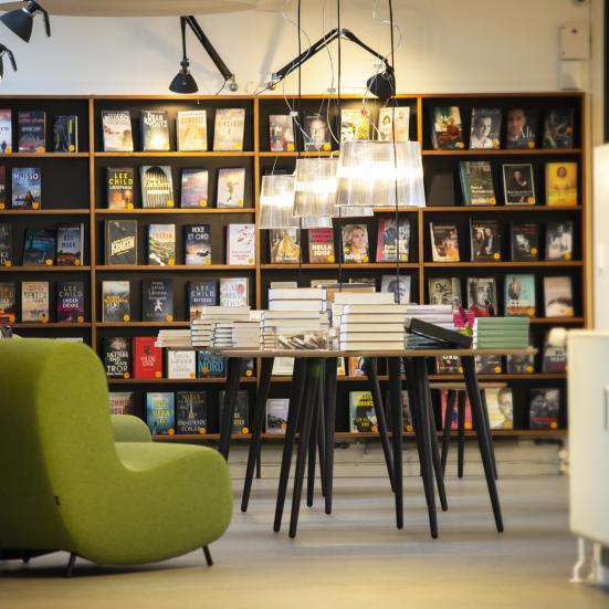 Biblioteket Godthåbsvej set indefra, hvor der står en grøn stol, et bord og en bogreol langs væggen.