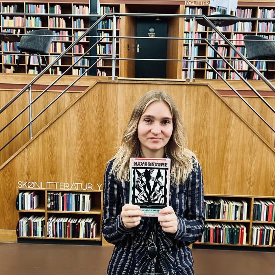 Litteraturformidler Amalie Pind stående med bogen Havbrevene i bibliotekssalen.