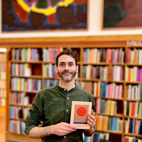 Billedet viser en mand som holder en bog foran nogle bogreoler på et bibliotek