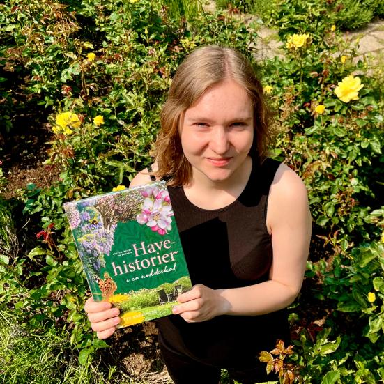Litteraturformidler Amalie i et rosenbed med med bogen Havehistorier i en nøddeskal.