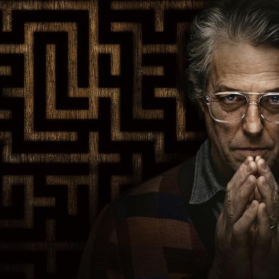 Billede af skuespilleren Hugh Grants ansigt på en mørk baggrund med et mønster. Han folder hænderne foran ansigtet.