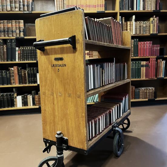 Historisk bogvogn i træ på en baggrund af fyldte bogreoler.