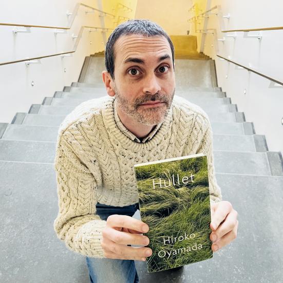 Billedet viser en mand på en trappe, og der holder bogen "Hullet" af Hiroko Oyamada