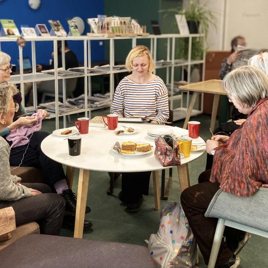 Højtlæsning for voksne, der sidder rundt om et bord med kage og kaffe