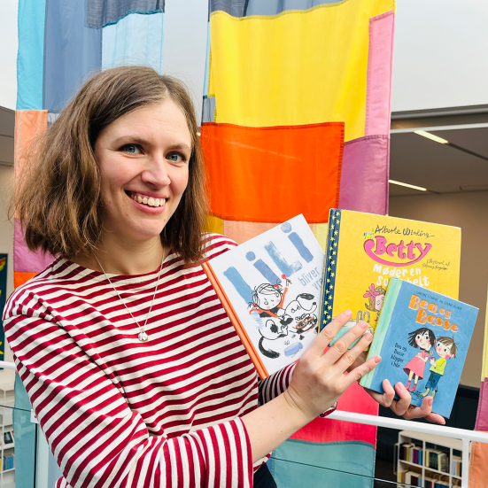 Bibliotekar holder de anbefalede bøger foran et farverigt bagtæppe