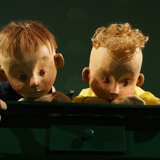 To dukker, der forestiller drenge kigger frem. Baggrunden er dunkel.