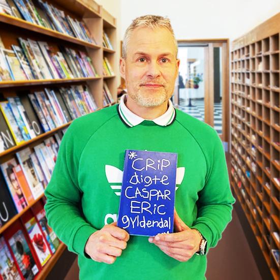 Bibliotekar i lysegrøn trøje stående med bogen 'Crips' mellem bogreoler