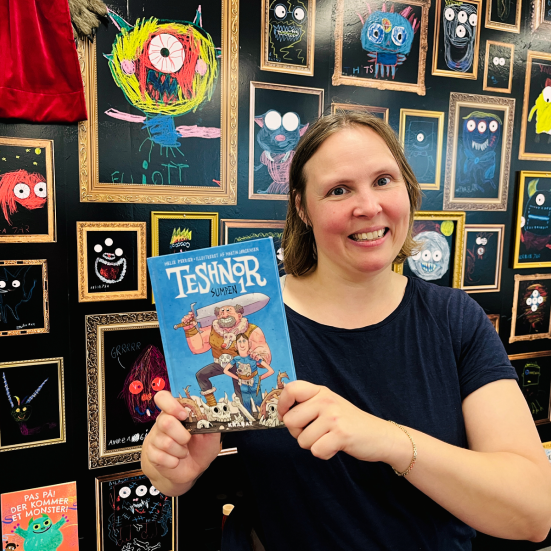 bibliotekar holder anbefalet bog. bagved er en væg med monstertegninger