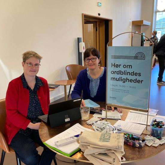 Billede af to kvindelige vejledere fra ordblindevejledningen siddende ved et bord på biblioteket
