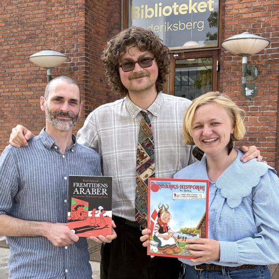 Tre litteraturformidlere med tegneserier i hænderne foran biblioteksbygning