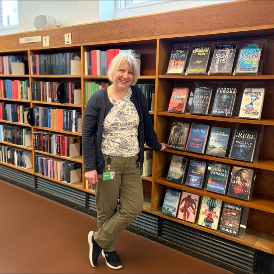 Bibliotekaren står foran reolerne med bibliotekets krimisamling