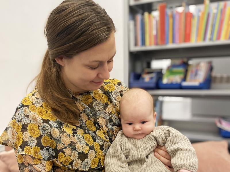 Mor med baby på skødet, der holder en bogn foran barnet