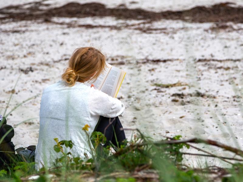 Pige på strand med bog