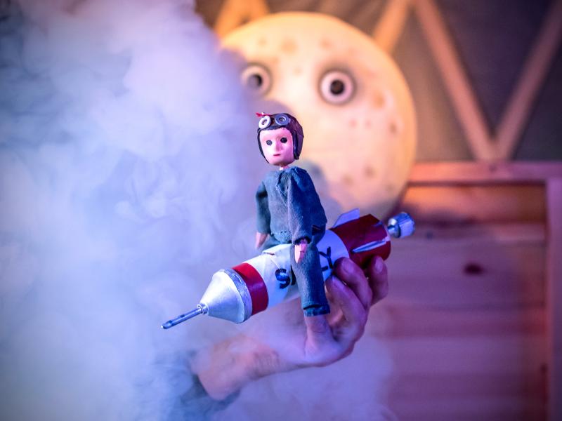 Billede af en dukke, der sidder på en raket. Billede fra forestillingen.