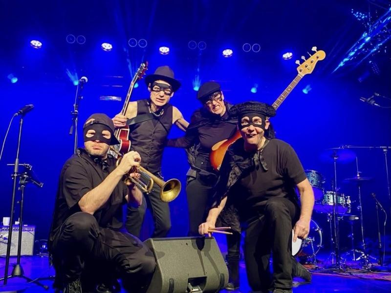 Fire musikere med skurkemasker på og blåt lys i baggrunden.