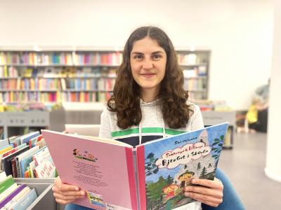 Oplæser sidder med bog i børnebiblioteket