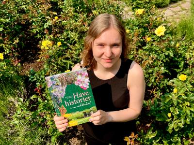 Litteraturformidler Amalie i et rosenbed med med bogen Havehistorier i en nøddeskal.