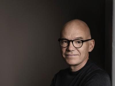 Forfatteren står med sort bluse og mørk baggrund med armene over kors.