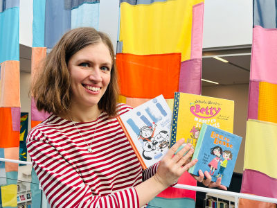 Bibliotekar holder de anbefalede bøger foran et farverigt bagtæppe