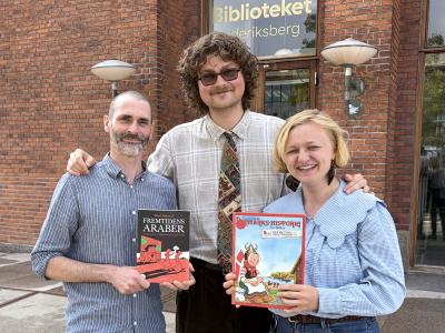Tre litteraturformidlere med tegneserier i hænderne foran biblioteksbygning