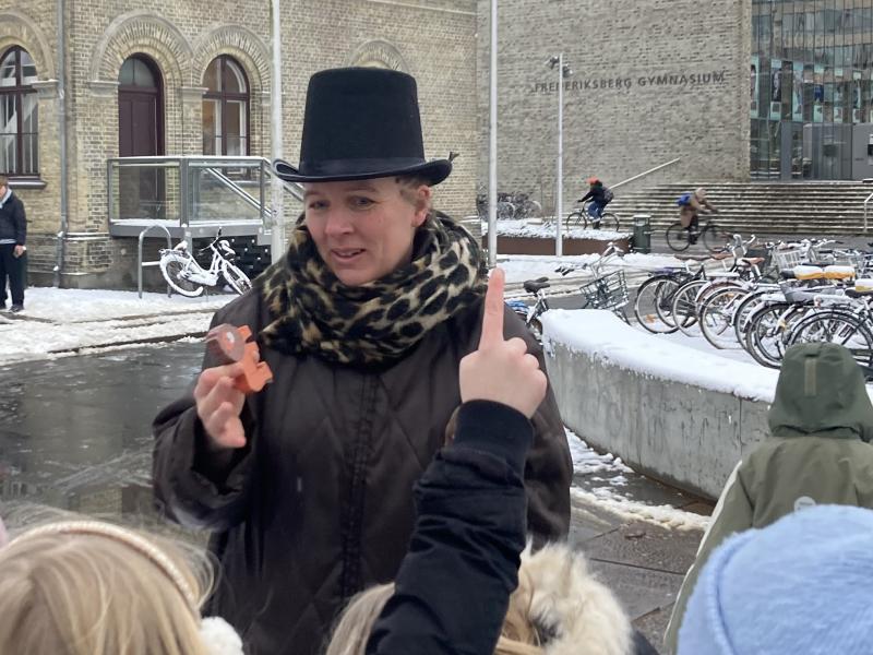 Fortæller på pladsen med børn med hænderne i vejret.