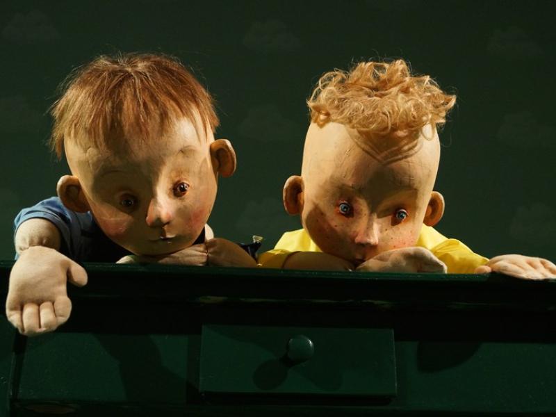 To dukker, der forestiller drenge kigger frem. Baggrunden er dunkel.