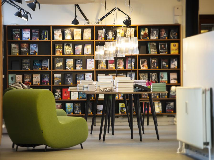 Biblioteket Godthåbsvej set indefra, hvor der står en grøn stol, et bord og en bogreol langs væggen.