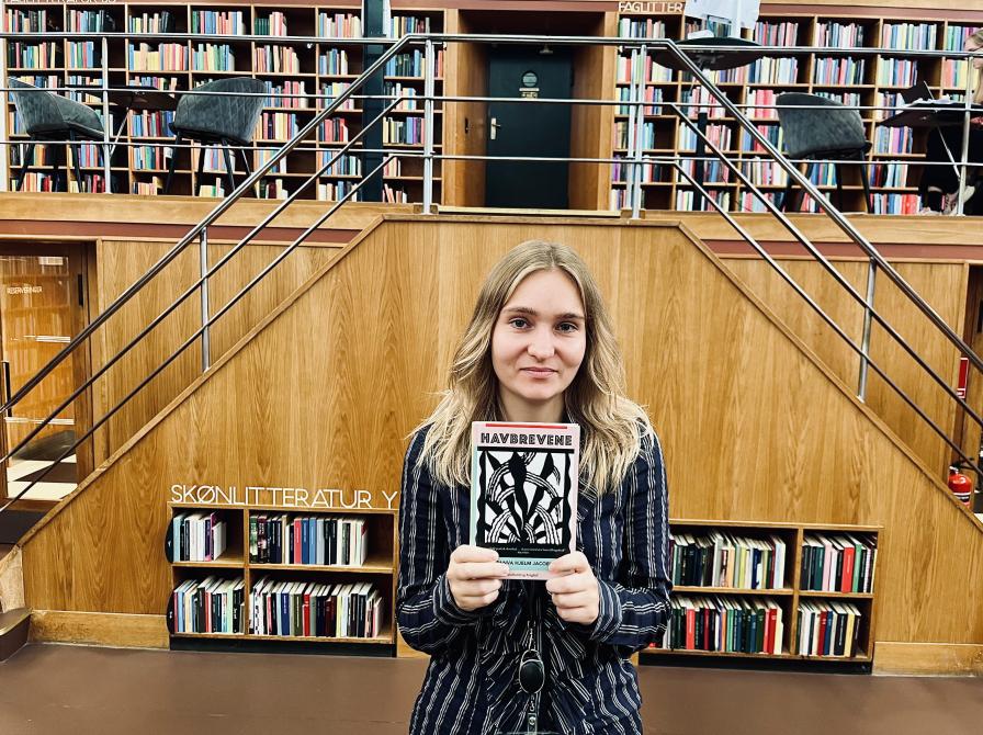 Litteraturformidler Amalie Pind stående med bogen Havbrevene i bibliotekssalen.