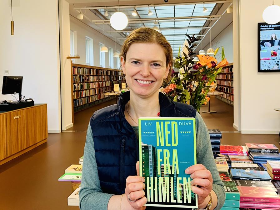 Litteraturformidler Helle Kundby stående med bogen 'Ned fra himlen' i bibliotekets lounge