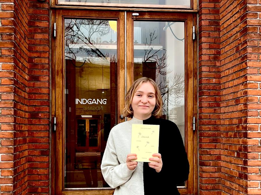 Litteraturformidler Amalie Pind med bogen Almanak foran bibliotekets indgang.