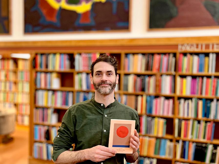 Billedet viser en mand som holder en bog foran nogle bogreoler på et bibliotek