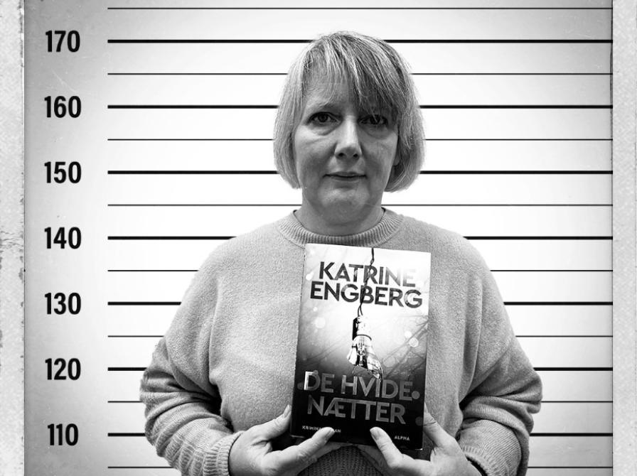Kvindelig bibliotekar stående med Katrine Engbergs krimi De hvide nætter foran en baggrund til kriminalfoto.