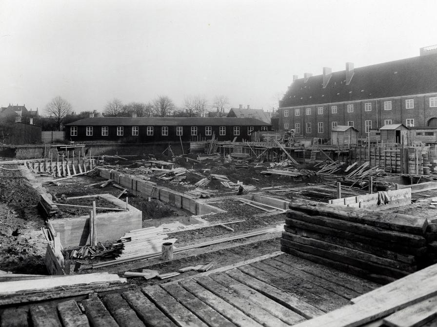 Byggepladsen, hvor den nye bygning så småt er undervejs. Bag fundamenterne ses biblioteksbarakken på Jernbanestien.