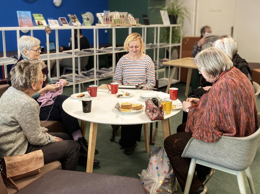 Højtlæsning for voksne, der sidder rundt om et bord med kage og kaffe
