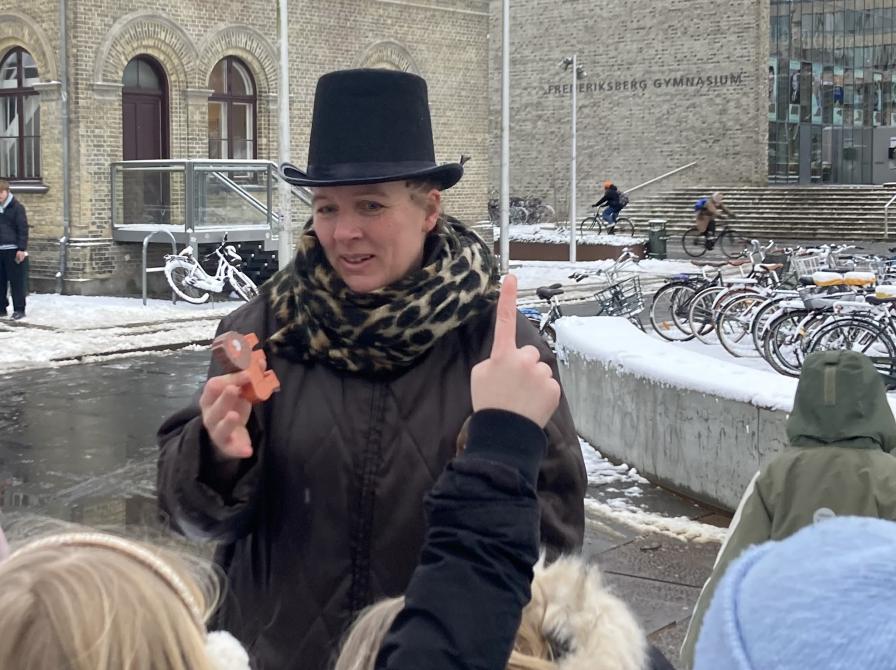 Fortæller på pladsen med børn med hænderne i vejret.