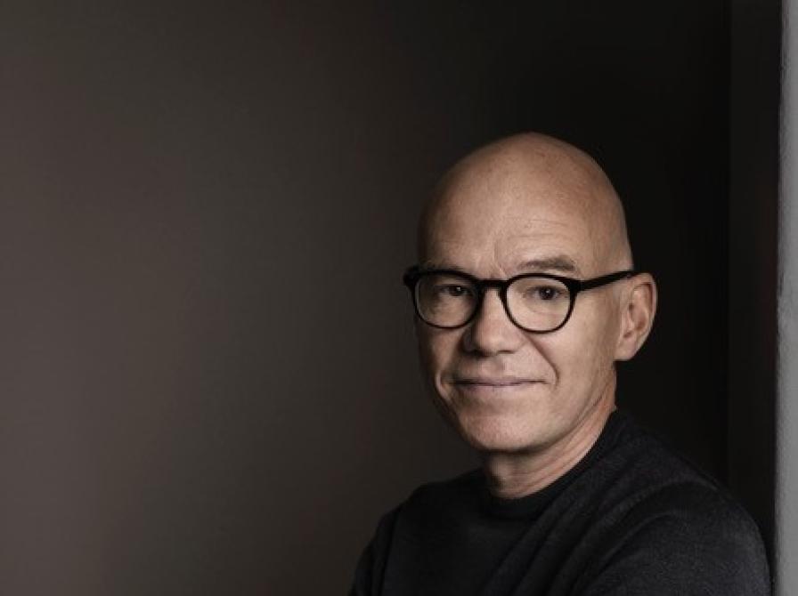 Forfatteren står med sort bluse og mørk baggrund med armene over kors.