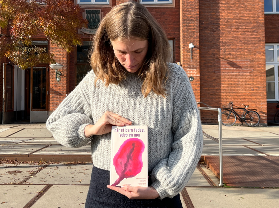 Bibliotekar står foran biblioteket og holder anbefalet bog