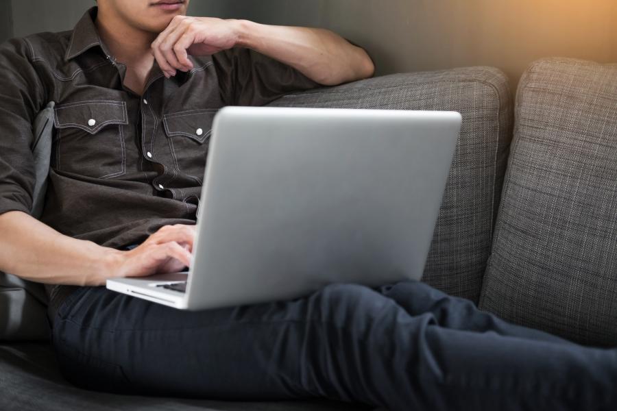 Ung mand sidder i sofa med en computer